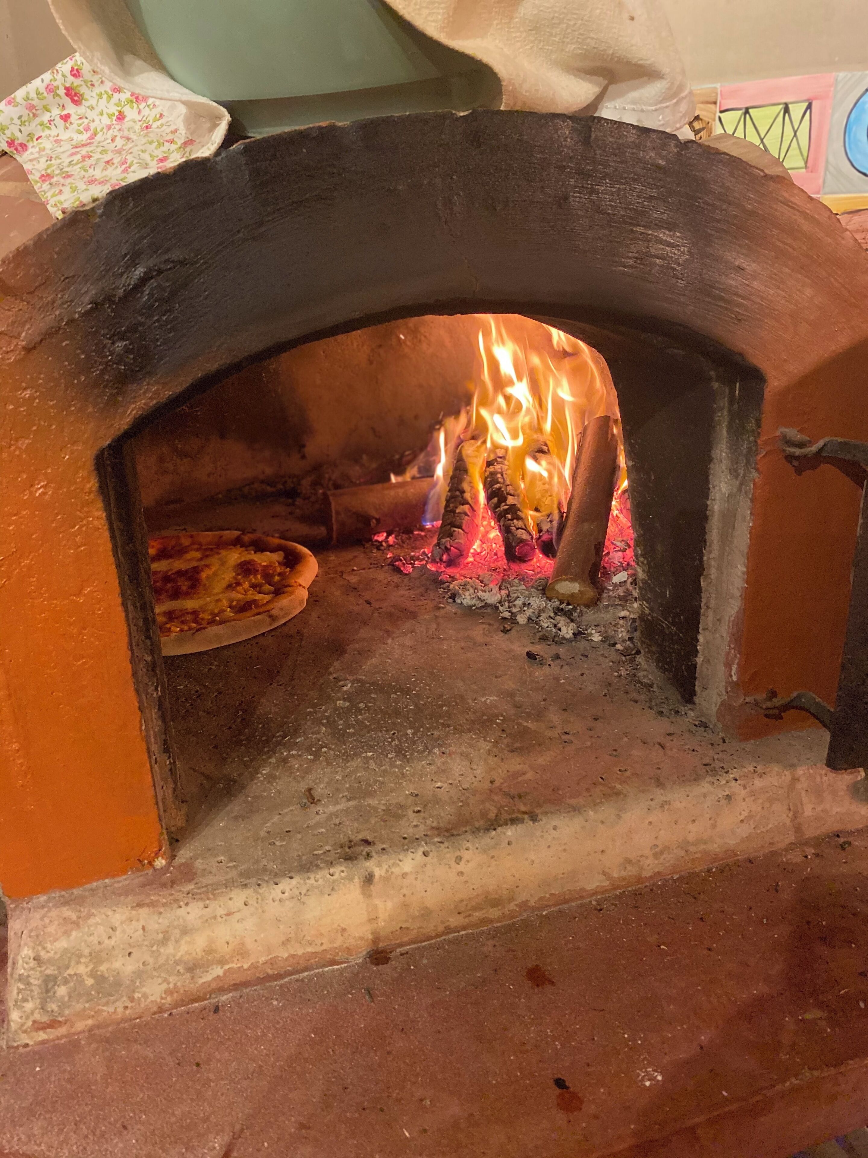 A pizza oven with a pizza inside, flames burning, and a rustic brick floor.