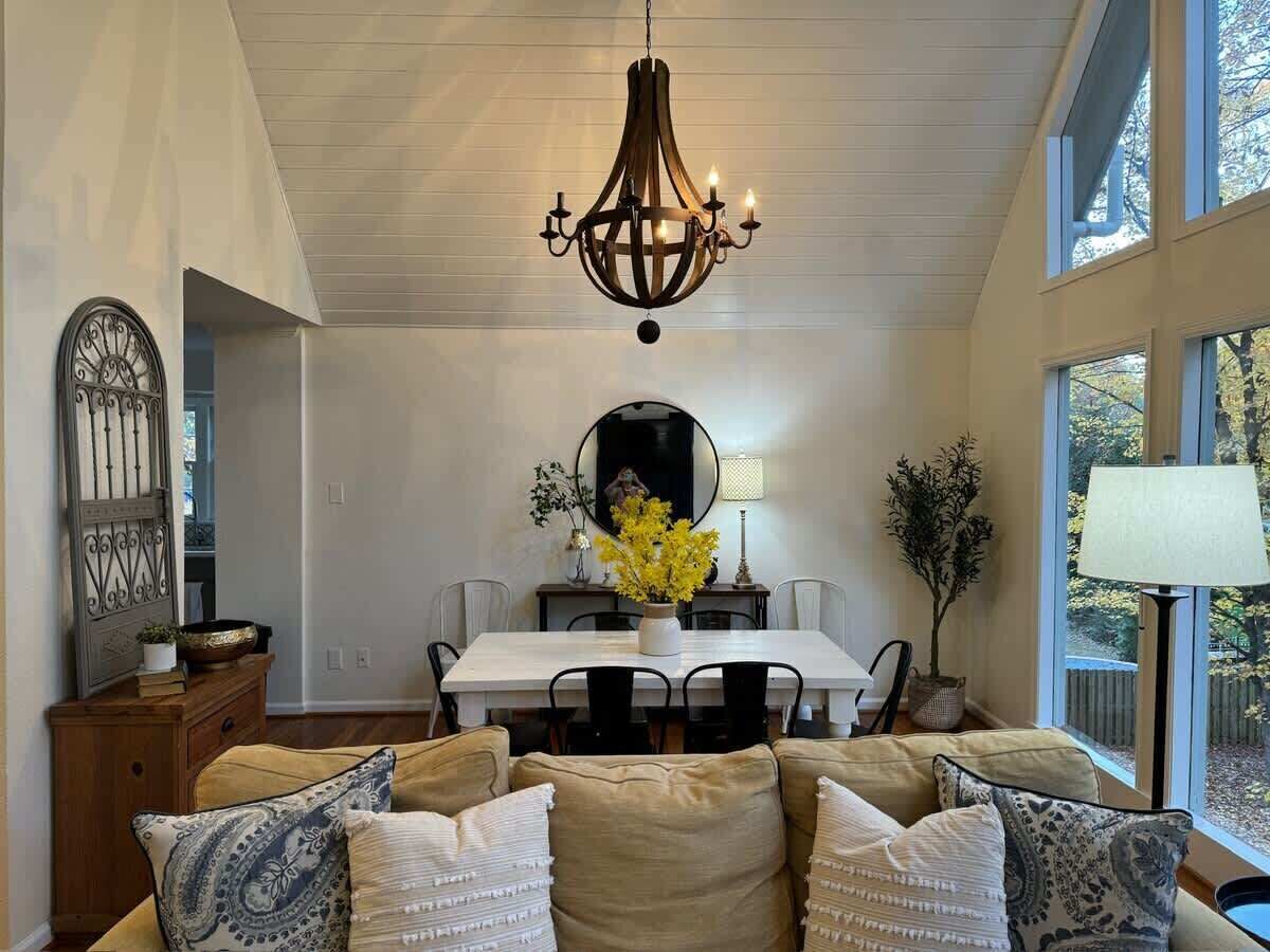 Zona pranzo con lampadario, tavolo da pranzo, sedie e un divano con cuscini decorati.