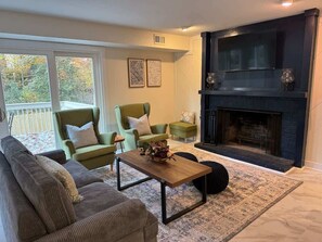 Un salon avec une cheminée, des fauteuils verts, un canapé et une table basse.