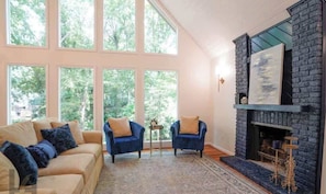 A living room with a large window, a fireplace, and a sofa. - North Hills Chalet with Game Room (Raleigh)