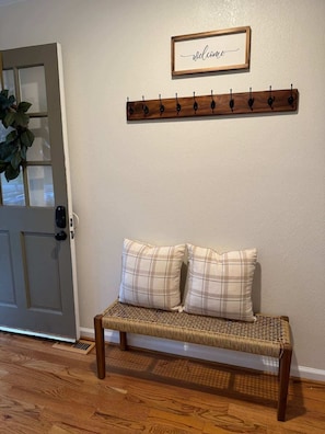 A wooden bench with two pillows, a coat rack with hooks, and a door with a window. - North Hills Chalet with Game Room (Raleigh)