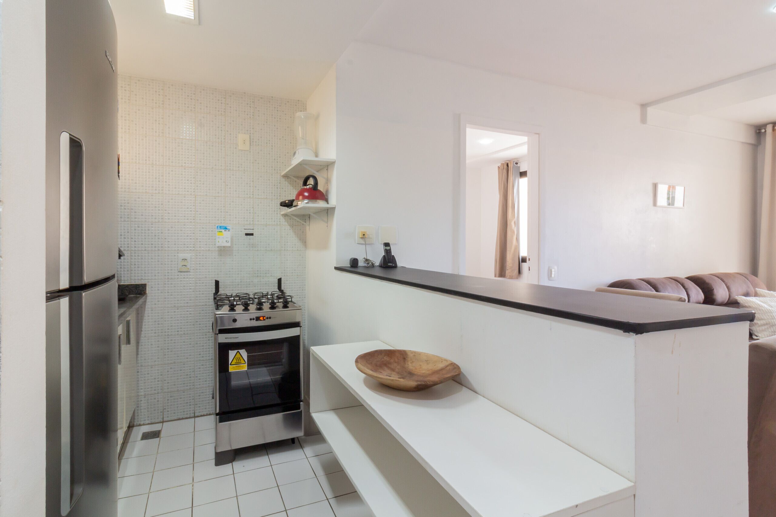 A modern kitchen with a built-in oven, a stove, and a wooden bowl on a white countertop.