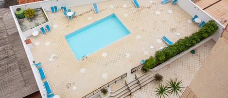 Vista aérea de un área de piscina en la azotea, con una piscina rectangular, varias sillas de descanso y una pequeña zona de estar.