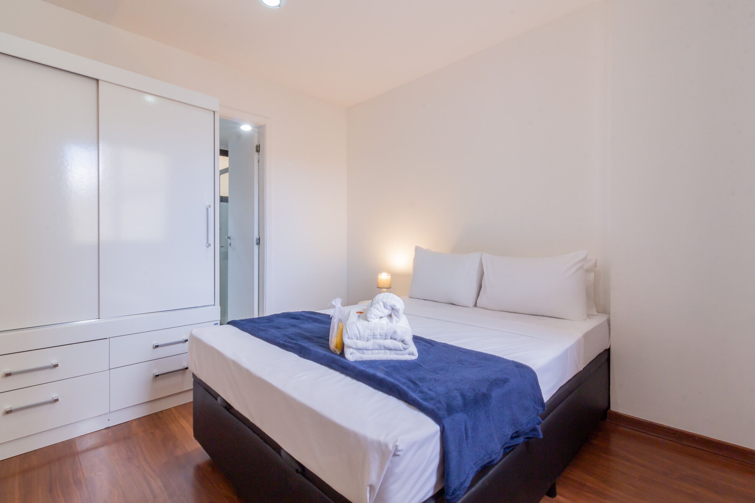 A bedroom with a bed, a wardrobe, and a bedside table with a lamp.