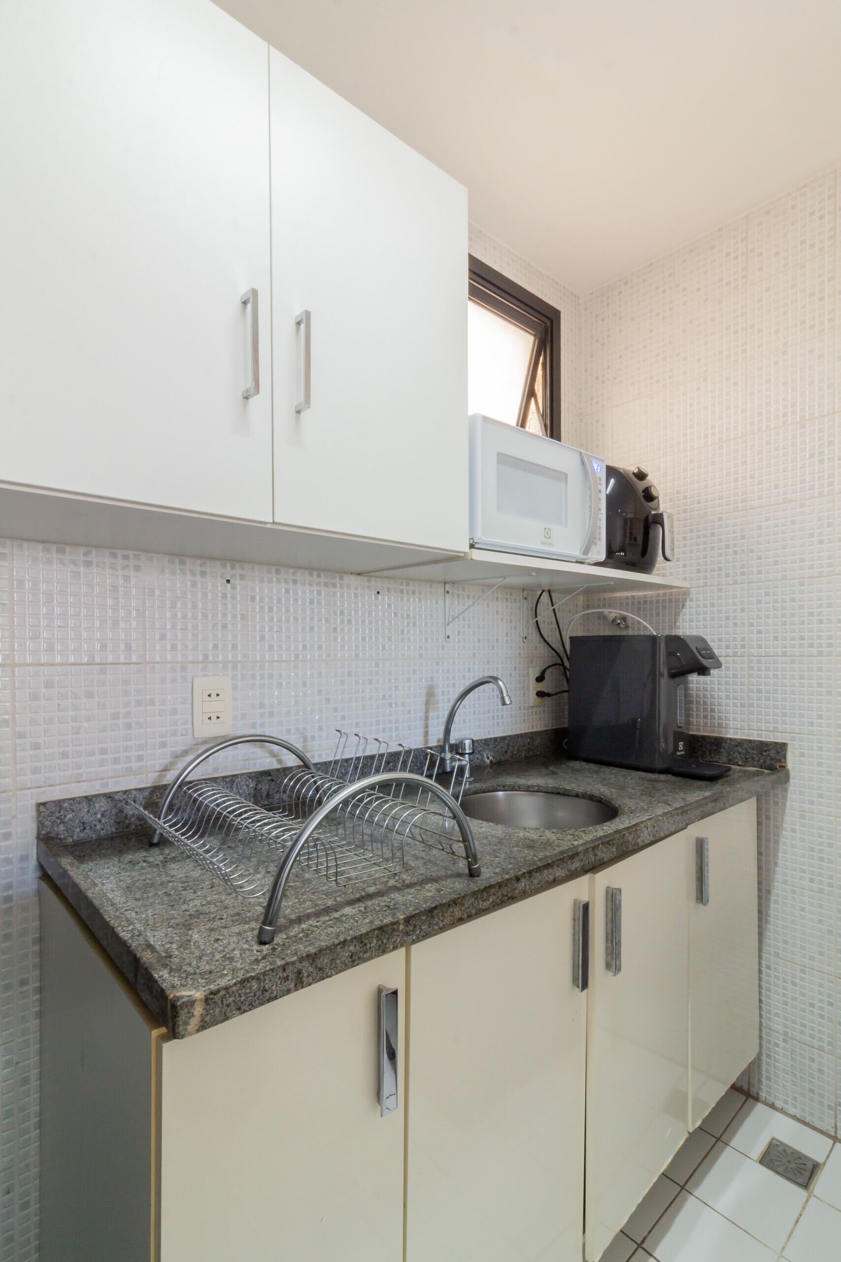 A kitchen with white cabinets, a granite countertop, a dish rack, a sink, a microwave, and a coffee maker.
