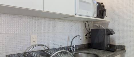 A kitchen with white cabinets, a granite countertop, a dish rack, a sink, a microwave, and a coffee maker.