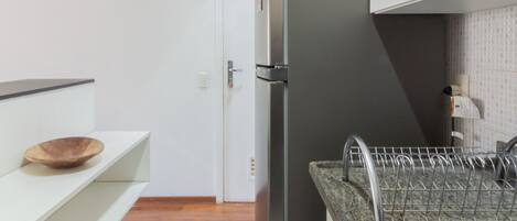 Una cocina con armarios blancos, un refrigerador de acero inoxidable, una encimera de granito y un cuenco de madera en un estante.