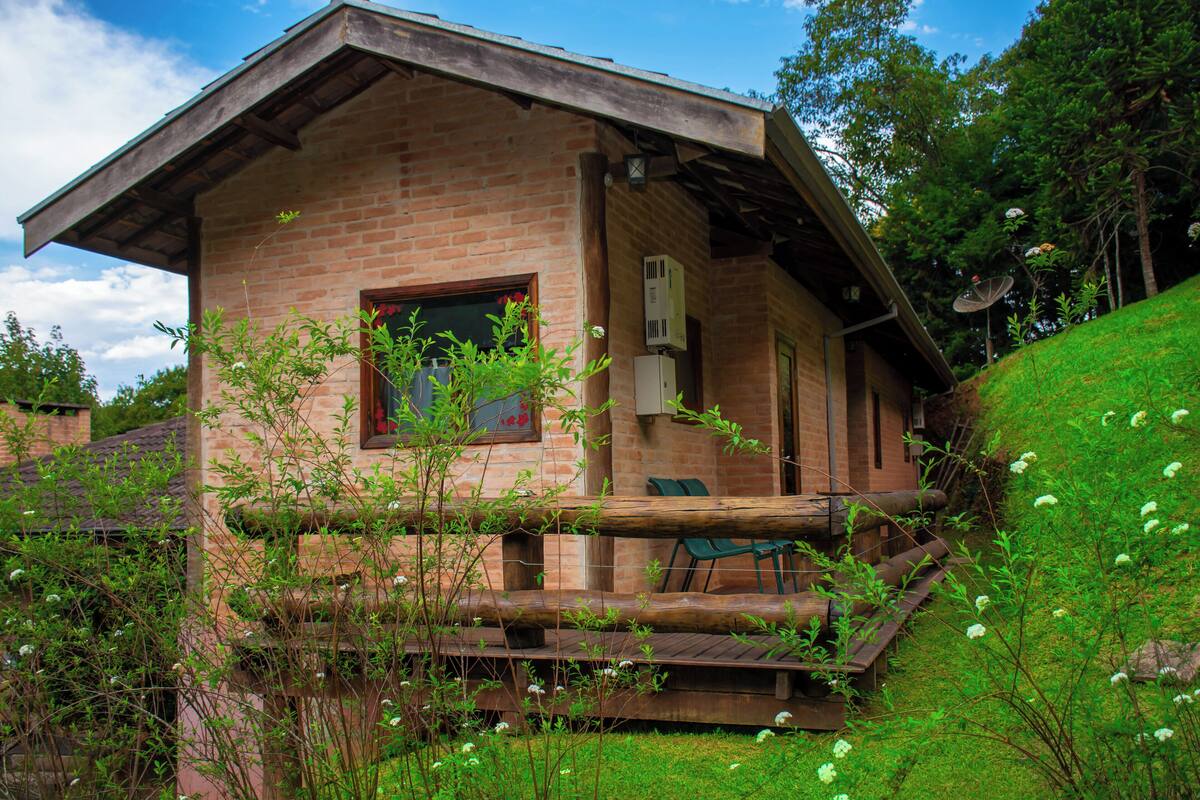 Une cabane rustique en bois, avec une façade en briques, une véranda dotée de chaises et une petite fenêtre.