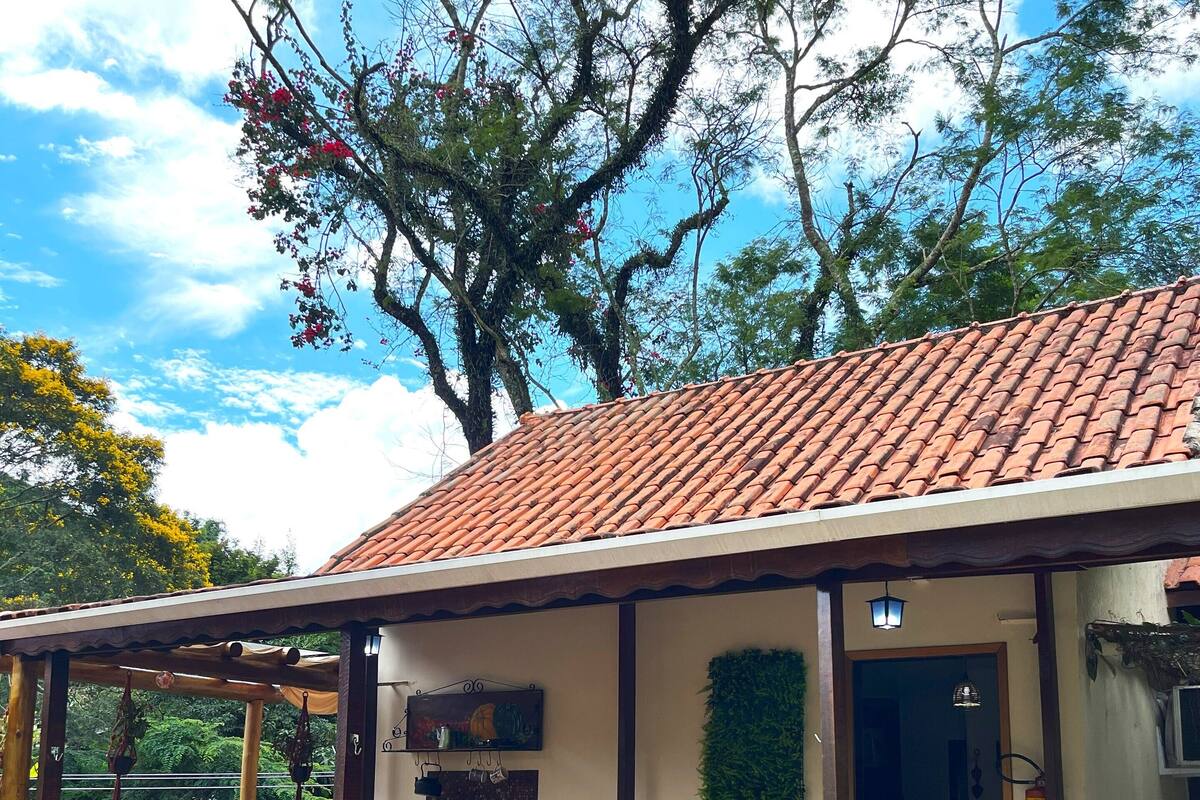 Une terrasse en bois avec des sièges d’extérieur, un toit en tuiles et une vue sur les arbres et le ciel.