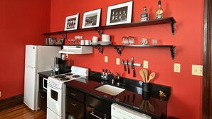 A compact kitchen with a white refrigerator, stove, and dishwasher, wooden flooring, and red walls. - Southern Charm and Comfort on the Bourbon Trail- Trail Suites Inn, Suite C (Lawrenceburg)