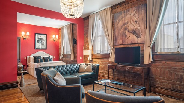 A modern living room with a large sofa, a coffee table, and a TV. There is a fireplace with a large painting above it. - Southern Charm and Comfort on the Bourbon Trail- Trail Suites Inn, Suite C (Lawrenceburg)