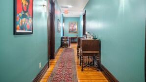 A hallway with teal walls, a wooden floor, a red patterned rug, a wooden table with a bowl, and framed artwork. - Southern Charm and Comfort on the Bourbon Trail- Trail Suites Inn, Suite C (Lawrenceburg)