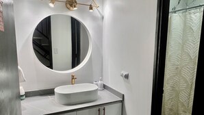 Ein Badezimmer mit rundem Spiegel, einem weißen Waschbecken und einer modernen Lampe darüber.
