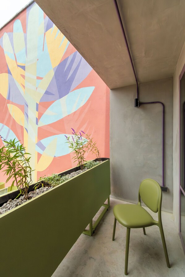 A balcony with a colorful mural, a green planter with plants, and a green chair.