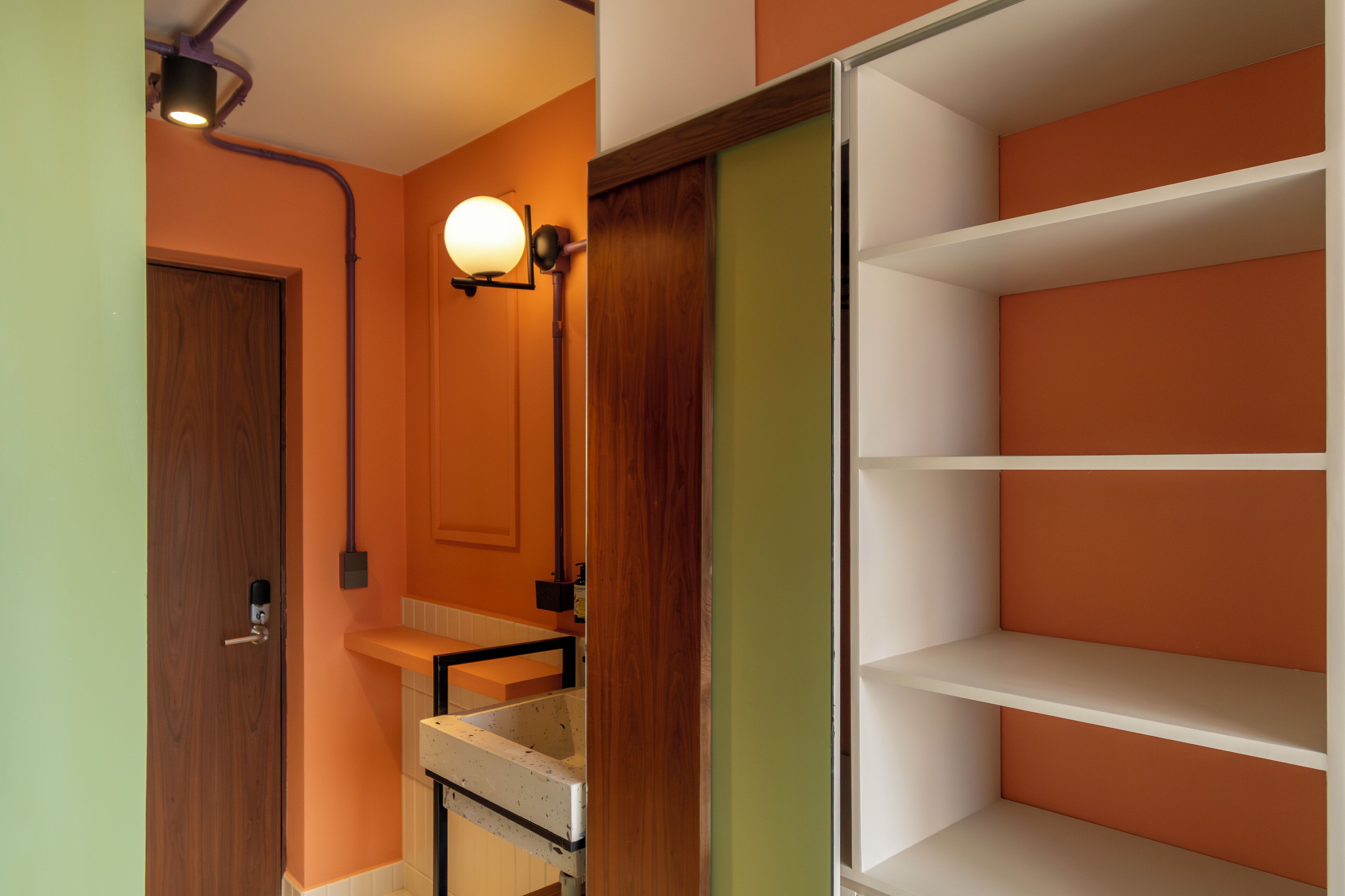 Un baño con puerta de madera, un lavamanos blanco, un espejo y un armario con varios compartimentos.