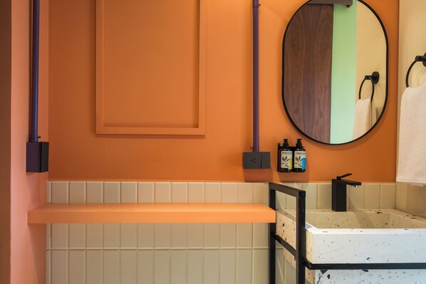 A bathroom with a white sink, a mirror, and a shelf. There are toiletries on the shelf.