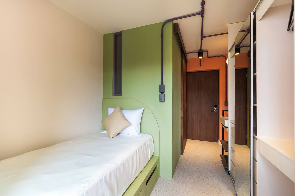 A bedroom with a bed, a green wall, and a wooden door.