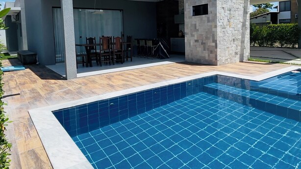 A modern house with a swimming pool, a patio with outdoor furniture, and a stone wall.