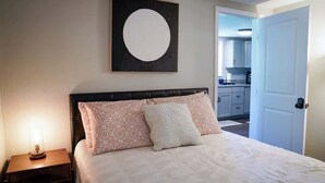 Una camera da letto con un letto, un comodino, un'opera d'arte appesa al muro e vista sulla cucina.