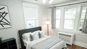 A bedroom with a bed, a bedside lamp, a radiator, and a window with curtains. - Hamilton Hideaway (Hagerstown, MD) (Hagerstown)