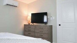 Une chambre à coucher comprenant un lit, une commode, un téléviseur et un appareil de climatisation.