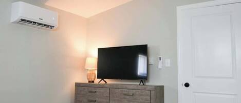Un dormitorio con cama, cómoda, televisor y aire acondicionado.
