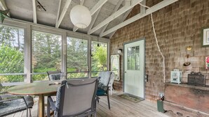 A covered outdoor area with a wooden deck, a table with chairs, and a door leading to the interior. - The Grounds - Brewster, MA (Brewster)