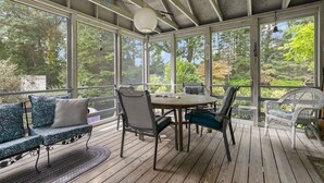 A covered outdoor deck with a wooden table and chairs, surrounded by cushioned seating. - The Grounds - Brewster, MA (Brewster)