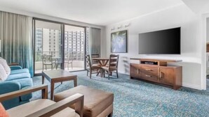 Habitación de hotel con un gran ventanal, un televisor de pantalla plana, un mueble de madera y una alfombra azul estampada.