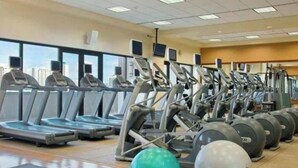 Un gimnasio con varias cintas de correr y pelotas de ejercicio, ventanas amplias con vista a la ciudad y suelo de baldosas.