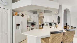 Une cuisine moderne avec des meubles blancs, un îlot central et des chaises en osier.