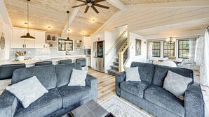 A spacious living area with two grey sofas, a wooden ceiling, and a kitchen in the background. - Canoes & Dock: Waterfront Retreat on Lake Beulah! (East Troy)