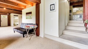 A spacious room with a sofa, a small table with books, a framed picture on the wall, and a staircase leading to a kitchen area. - Fire Pits & Grill: Lakefront Jackson Home (Jackson)