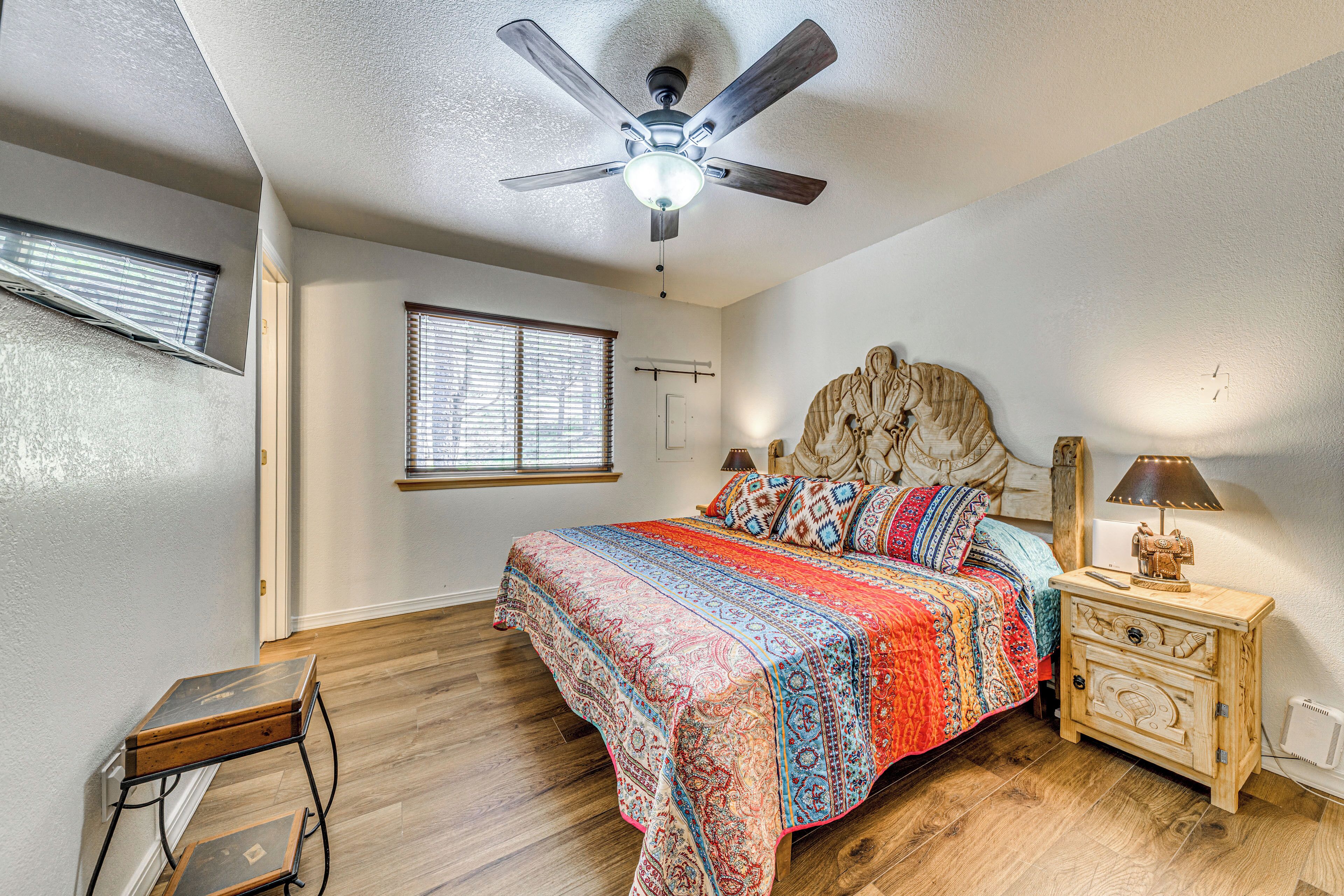 A bedroom with a bed, a nightstand, a ceiling fan, a window, and a wooden floor.