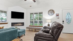 Una sala de estar con televisor de pantalla plana, chimenea, sofá de cuero y ventilador de techo.