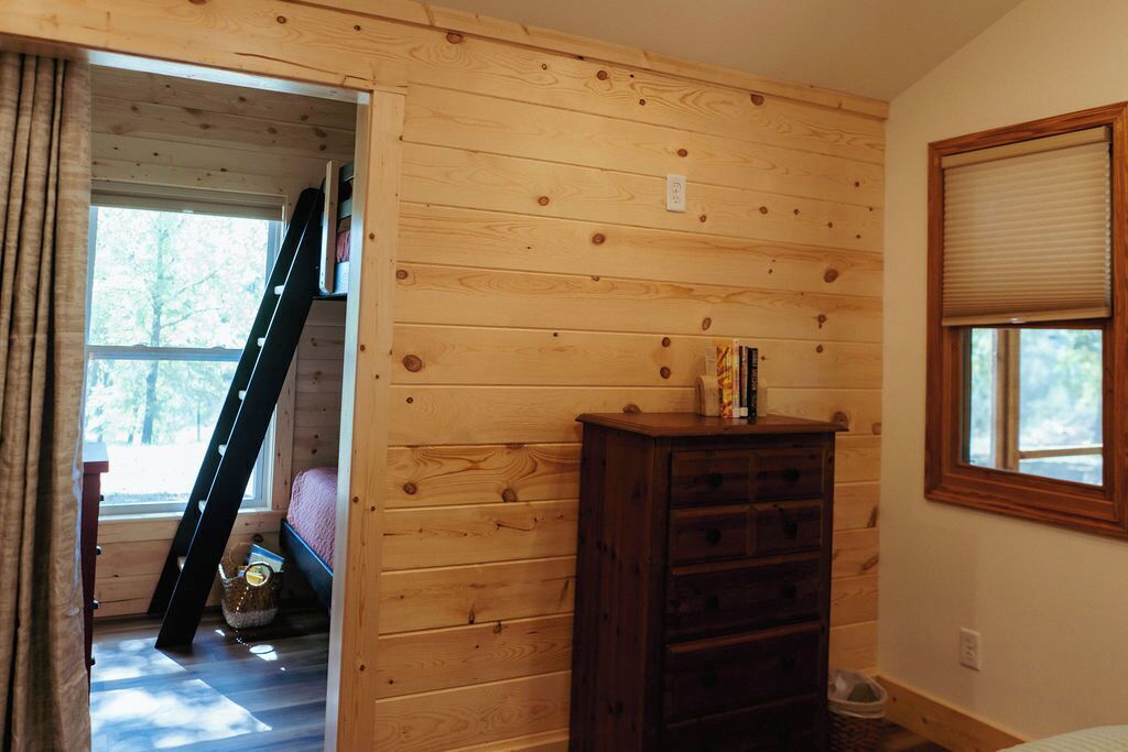 Ein Zimmer mit Holzwänden, einem Bett, einem Schminktisch und einem Fenster mit Jalousien.