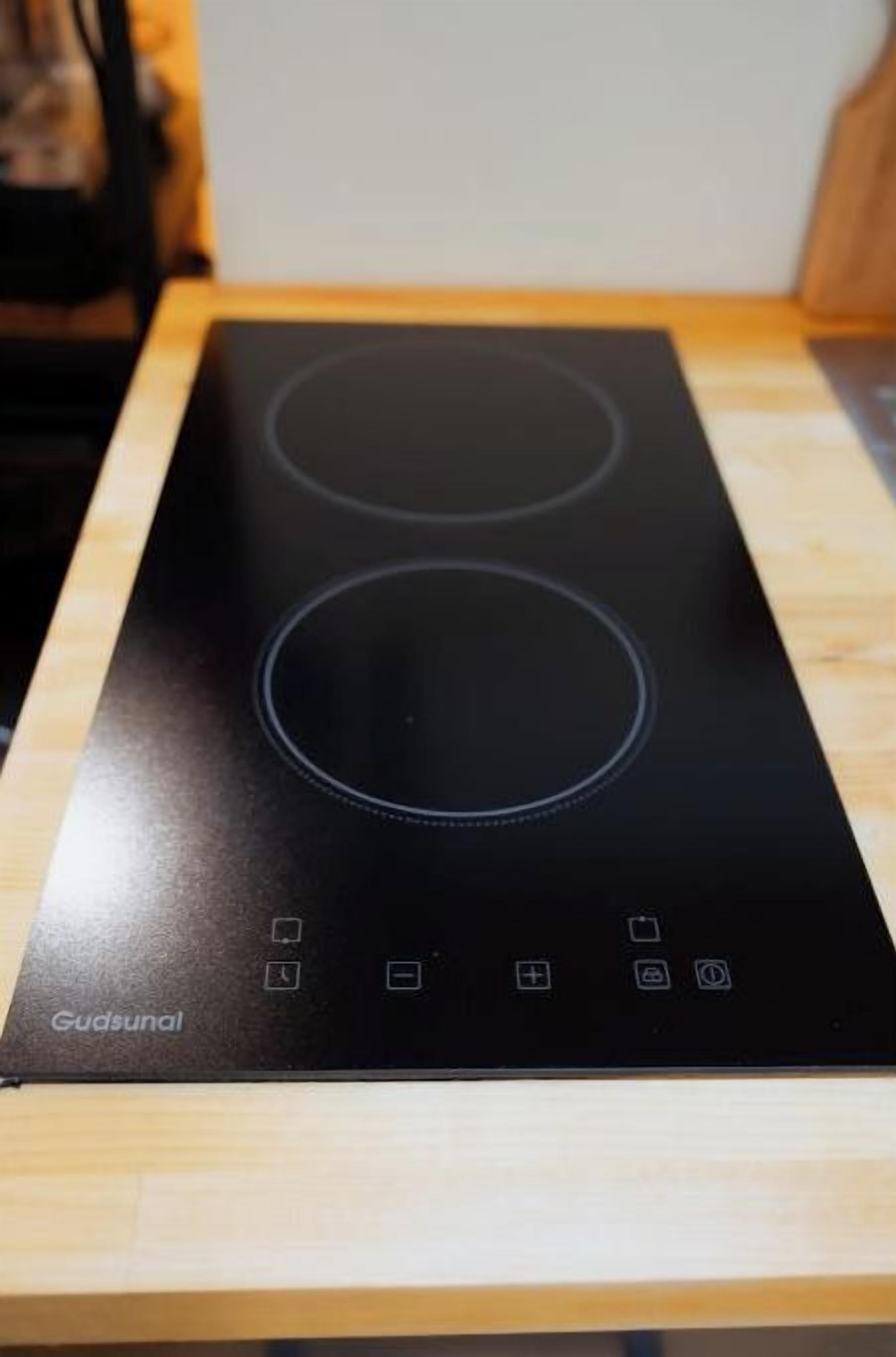 A black induction cooktop with a control panel on a wooden countertop.