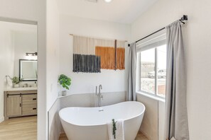 Un baño moderno con una bañera independiente, un espejo grande y un ventanal con cortinas.
