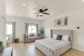 Un dormitorio moderno con cama, sofá, ventilador de techo y ventana con cortinas.