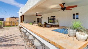 Ein Außenbereich mit Bar, Pool, Barhocker, Deckenventilatoren und Topfpflanzen.