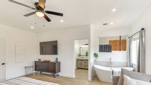 Ein modernes Schlafzimmer mit Bett, Kommode, Deckenventilator und einem Badezimmer mit Badewanne und Dusche.