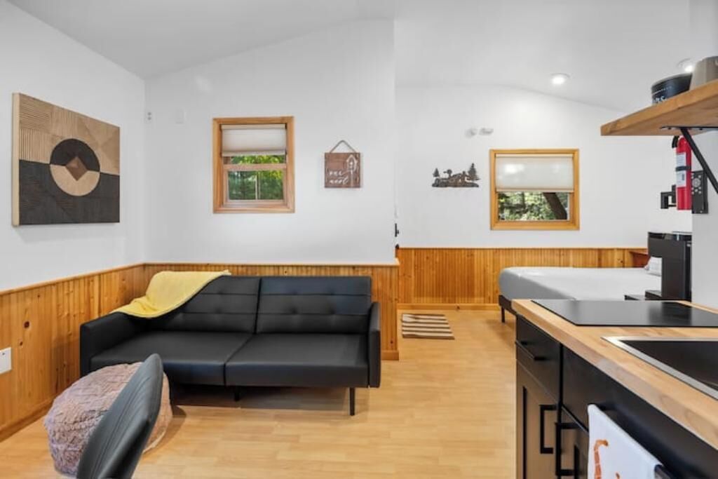 Una stanza moderna con un divano nero, pannelli in legno, un angolo cottura con lavello e piano cottura, e opere d'arte alle pareti.