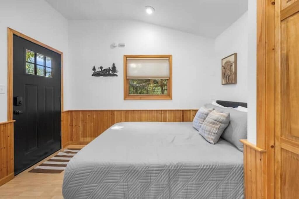 A bedroom with a bed, a window, a door, and a small wall decoration.