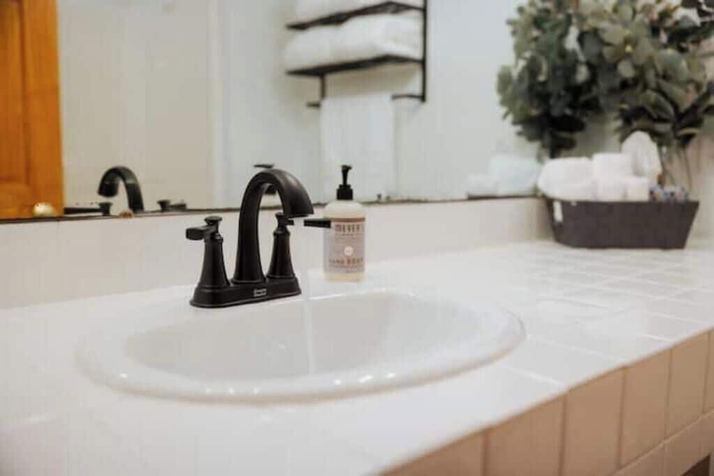 A bathroom with a white sink, black faucet, and a bottle of hand soap.