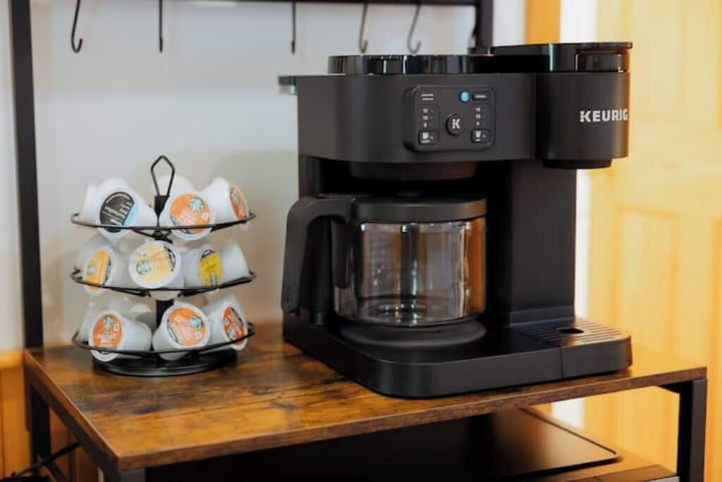 Une machine à café Keurig posée sur une table en bois, avec un plateau rempli de gobelets à café jetables.