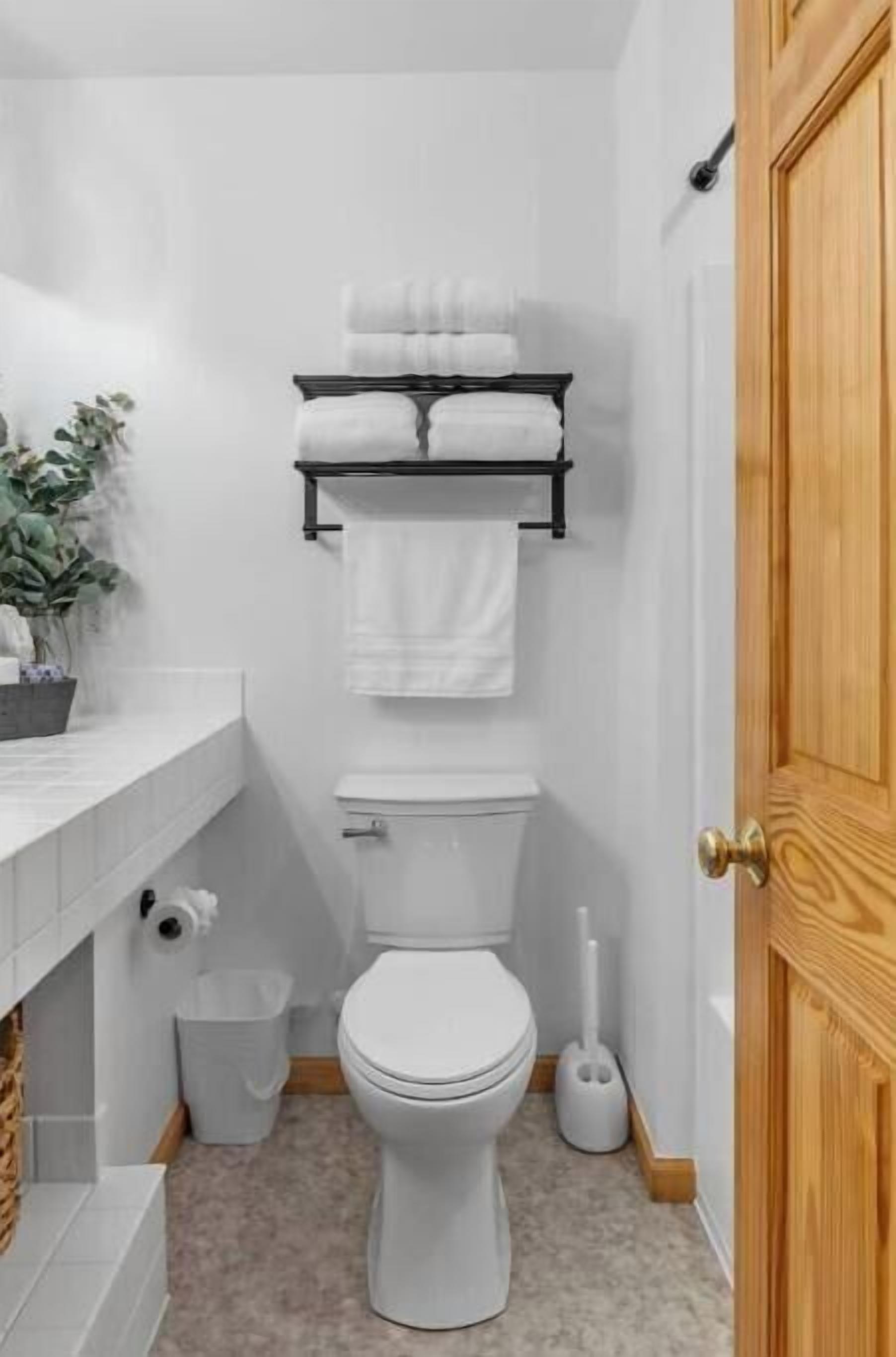 Une petite salle de bain propre, équipée de toilettes, d’un porte-serviettes, d’une poubelle et d’une brosse pour les toilettes.