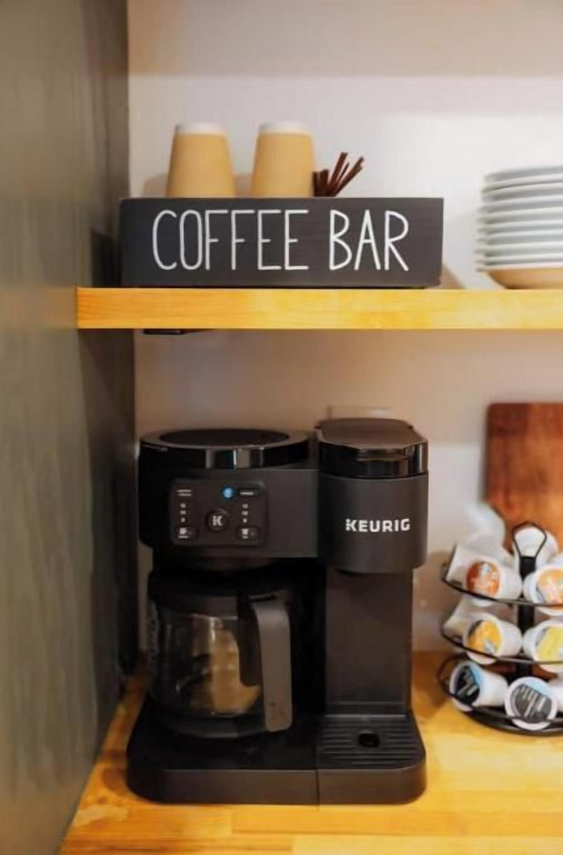 Une machine à café posée sur une surface en bois, avec une pancarte au-dessus indiquant « CAFÉ ».
