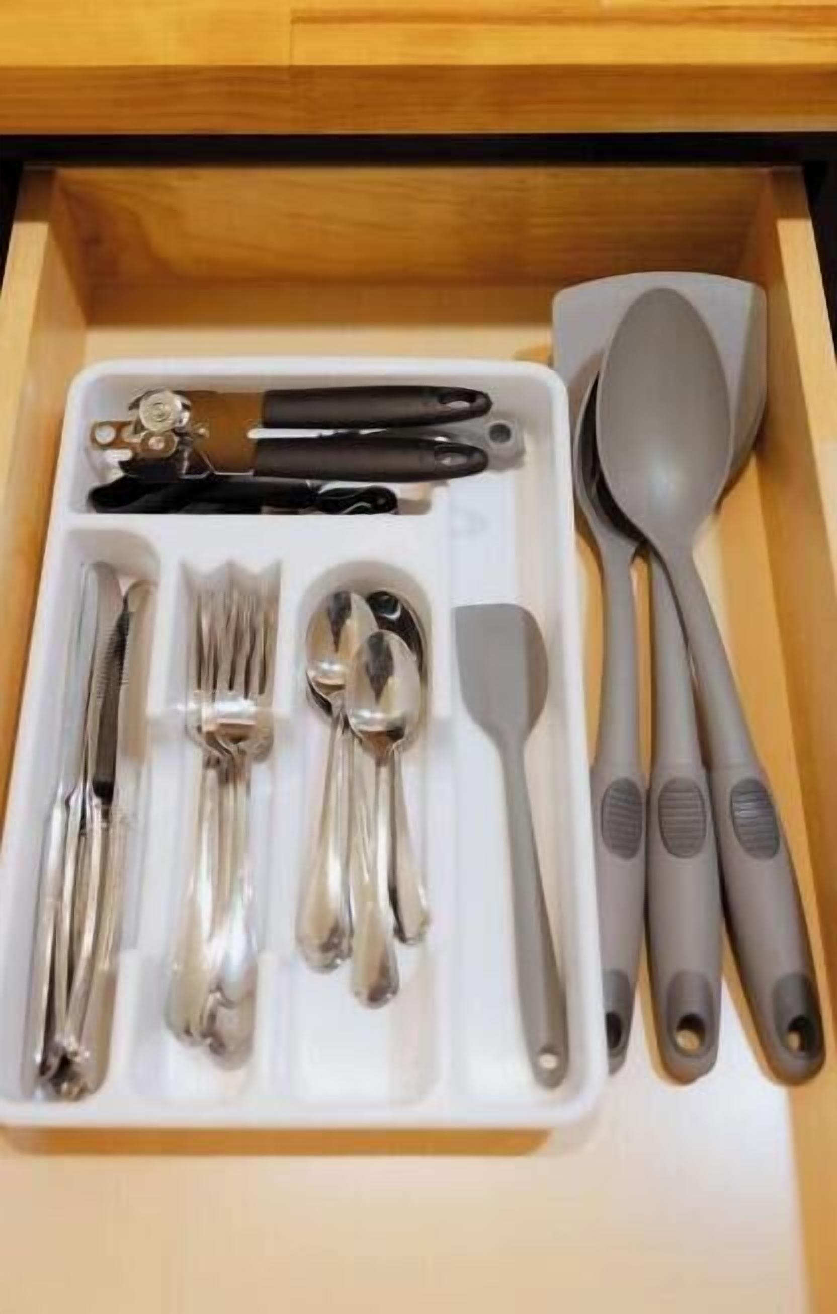Un cajón con cubiertos, incluyendo tenedores, cucharas y un cuchillo, ordenados en una bandeja blanca.