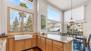 A modern kitchen with wooden cabinets, a large island, and a dining area with chairs and a table. - Mountain Retreat Near Skiing & Golf w/ Views (Silverthorne)