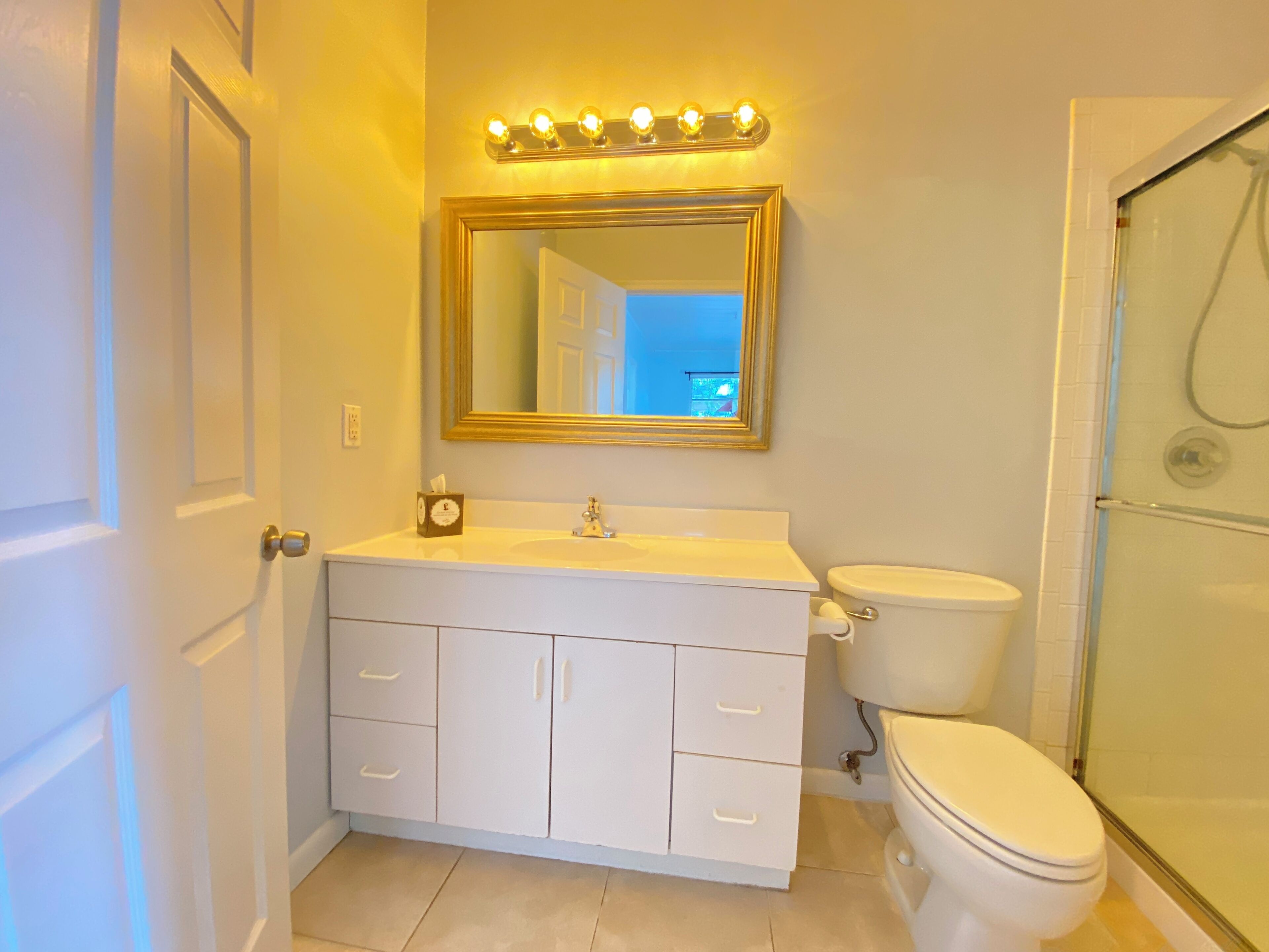 A bathroom with a white vanity, a gold-framed mirror, and a shower area.